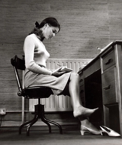 Female office worker sitting taking notes. Writing barefoot  /  taking shoe