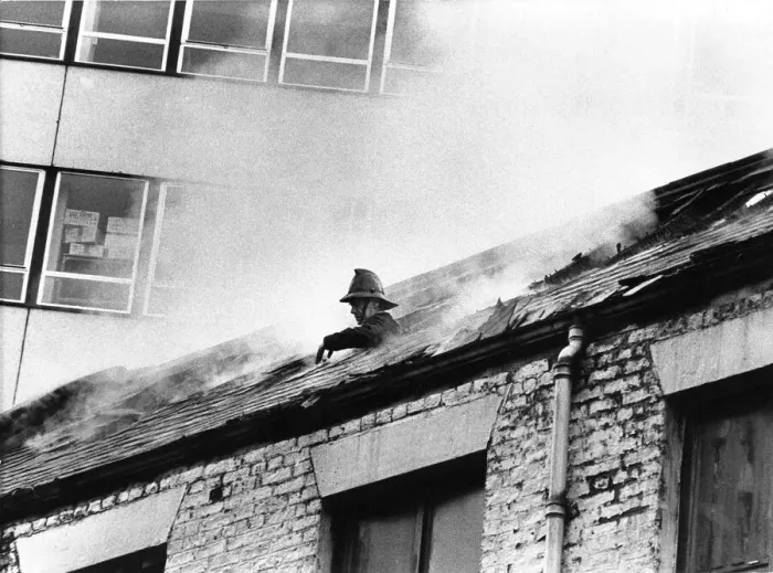Framed Print : A firefighter pokes his head through the roof of the smoke filled building to grab some Framed Print : A firefighter pokes his head through the roof of the smoke filled building to grab some