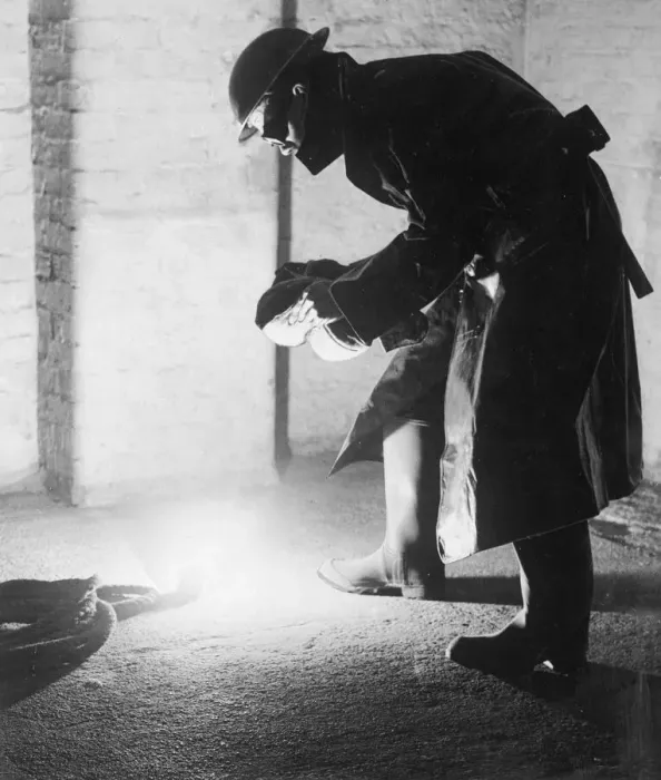 Framed Print : A firefighter tackles an incendary bomb with a sandbag which protects his face from Framed Print : A firefighter tackles an incendary bomb with a sandbag which protects his face from