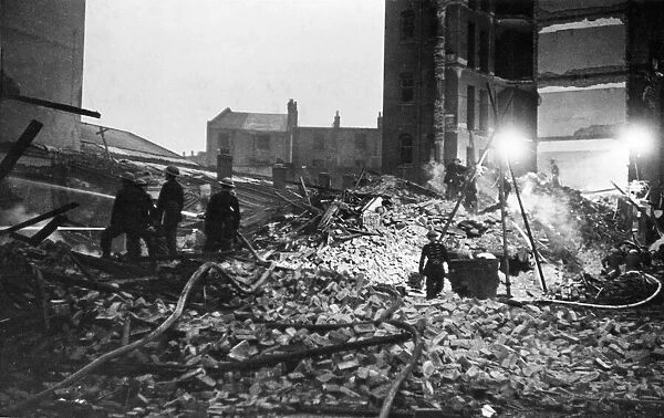 Firemen hosing the smouldering ruins of a factory, whilst still searching for