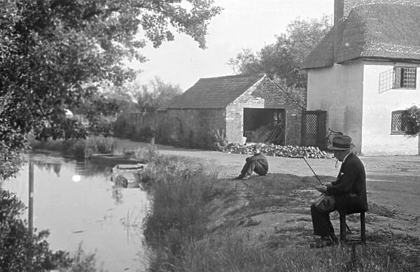 A fisherman prepares his rod beside a river in Kent. Circa 1946