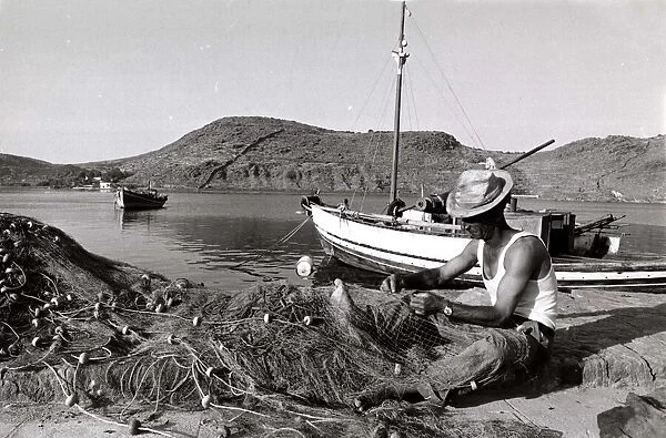 fisherman tends to his nets in Greece - fishing boat mountains river