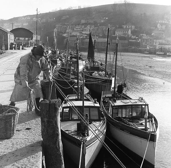 Fisherman ties his boat up in the harbour at Looe, Cornwall. Circa 1953