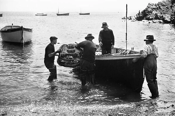 Fishermen loading lobster pots on to a small boat at Cadgwith. July 1939