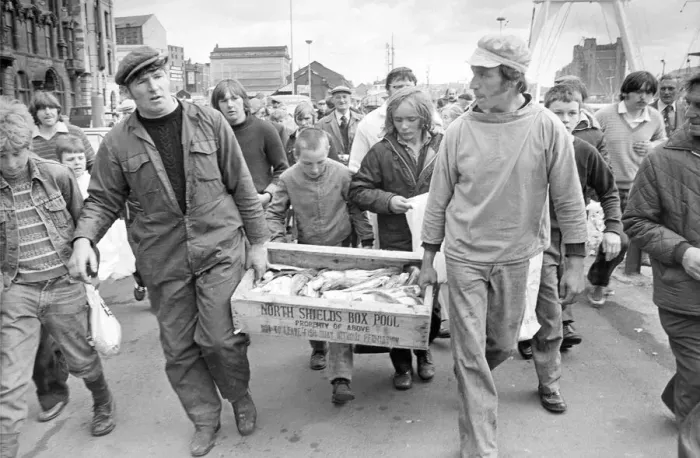 Framed Print : Two fishermen pursued by an eager crowd, bring a box of fish ashore in 1980