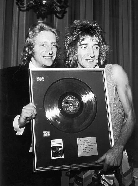 Footballer Denis Law presents singer Rod Stewart of The Faces with a gold disc to mark