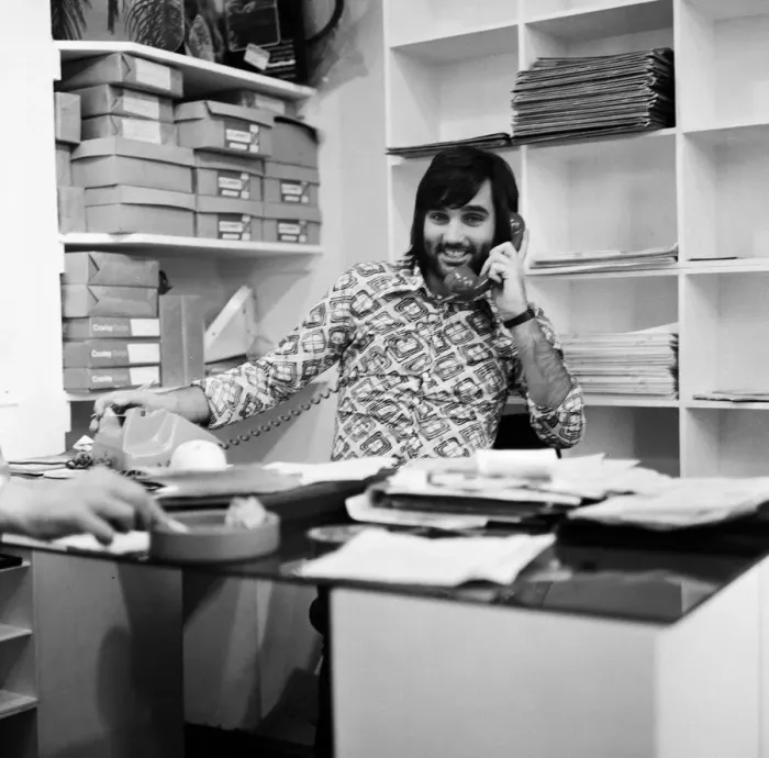 Framed Print : Footballer George Best, business man on the phone sitting at desk in his shop