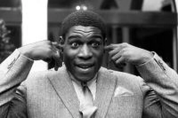 Frank Bruno stands with his hands raised and his fingers in his ears