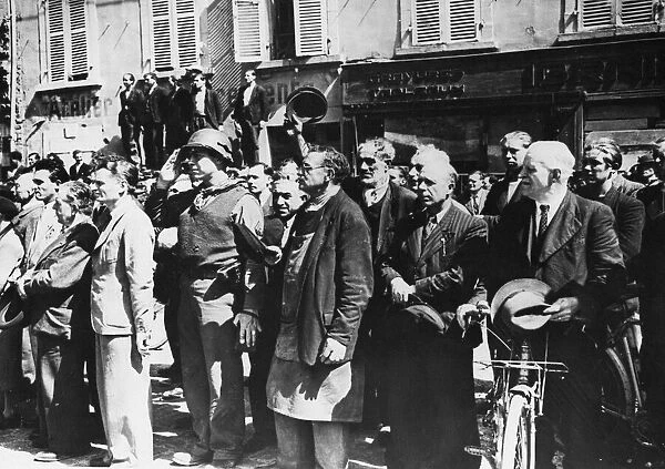 French civilians stand at attention and a GI salutes the American flag in Cherbourg