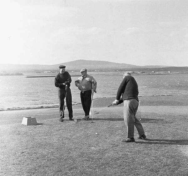 Three friends tee off for a round of golf on a very windy Fort Island Golf links Hotel