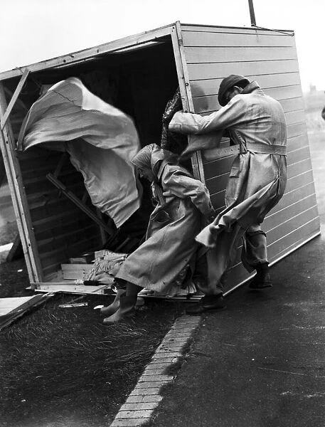 Gale damage. A couple cling desperately to their overturned beach hut at Littlehampton to