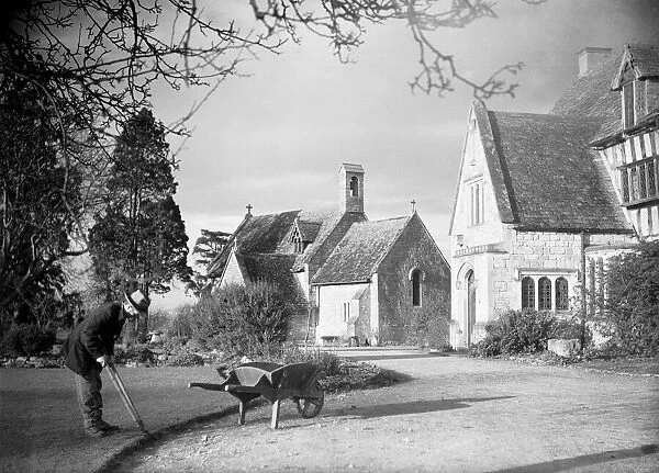A gardener trims the edge of the front lawn at a country house. January 1935