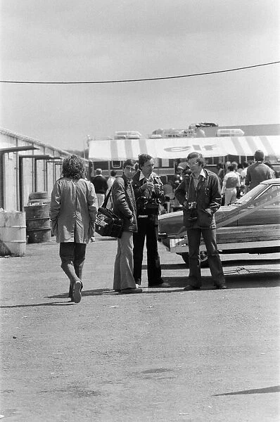 George Harrison walking past some photographers at the British Grand Prix motor racing