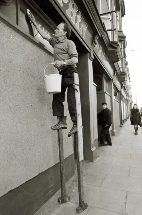 Framed Print : George Pettican Window Cleaner on Stilts cleaning windows on the front of his shop in Framed Print : George Pettican Window Cleaner on Stilts cleaning windows on the front of his shop in