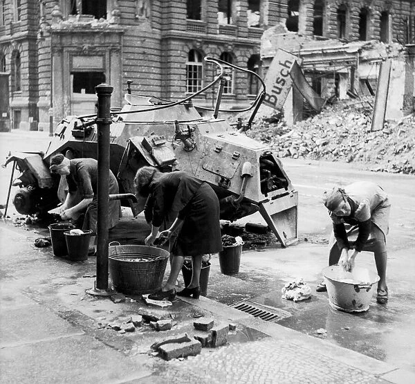 German women doing their washing in cold water in a street beside a knocked out German