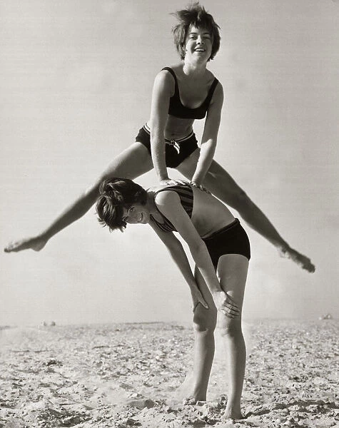 A girl performs an acrobatic leap frog over her friend as they play together on the beach