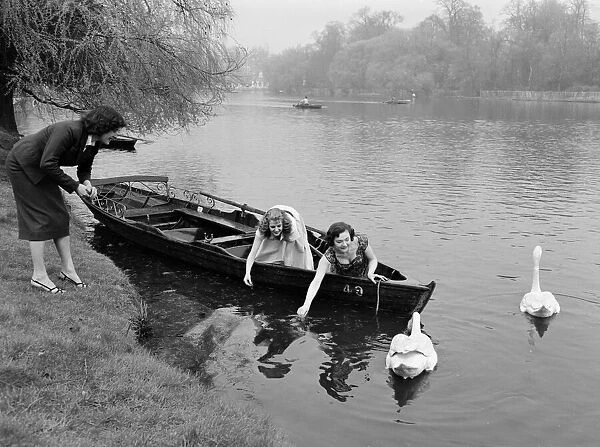 Girls feeding swans from their rowing boat after being out for a trip on the river