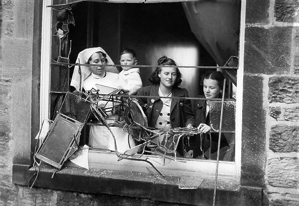 Girls and a nurse holding a litte baby looking out through the smashed window of a bomb