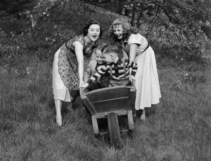 Framed Print : Two girls rolling two small boys down the hill in a wheelbarrow on a pleasant Spring day