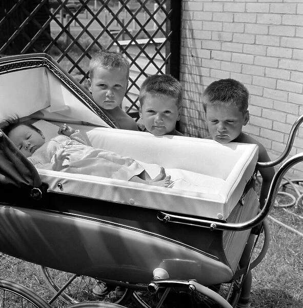 Three gloomy-faced triplet brothers aleaning over the side of a pram in the garden of
