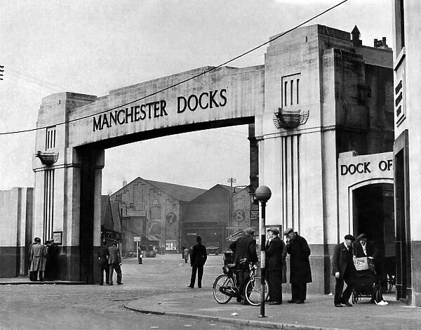 Only a few groups of men stand chatting at the gate of a deserted Manchester dock May