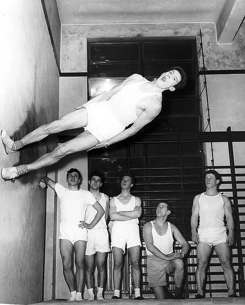 Gymnast Ken Popplewell walking on a wall watched by other members of the Ilford gymnastic