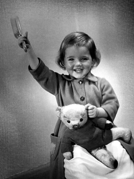 Happy young girl holding up her hairbrush after getting her teddy bear clothed