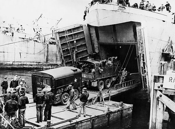 A heavy truck pulls a field kitchen up the bow ramp of an LST (Landing Ship Tank