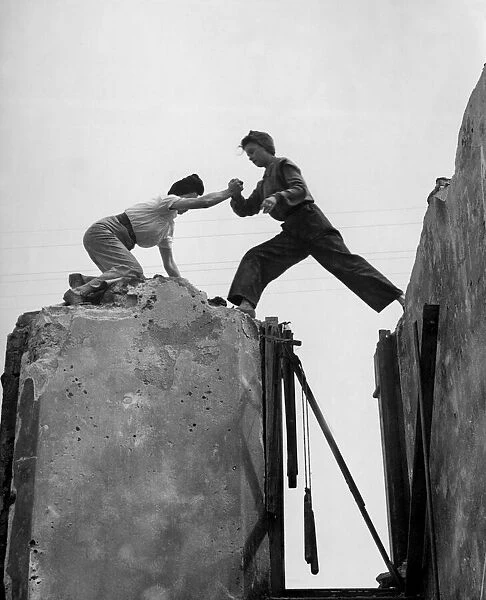 High up on the tottering wall, Lydia Walker steps across the gap aided by Betty Baker
