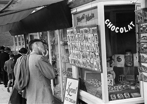Holiday scenes at Hastings. Holidaymaker looking at saucy postcards in a newsagents