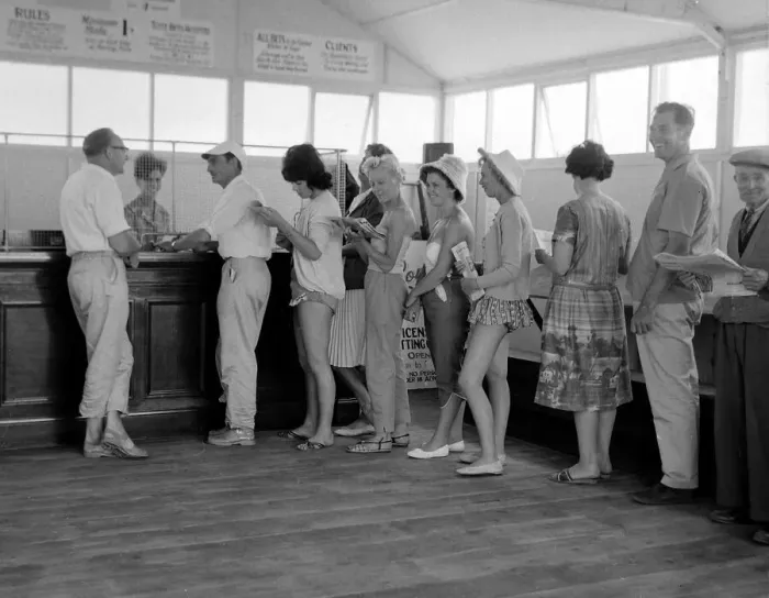 Framed Print : Holidaymakers line up to make a bet at a betting shop in the form of a wooden chalet Framed Print : Holidaymakers line up to make a bet at a betting shop in the form of a wooden chalet