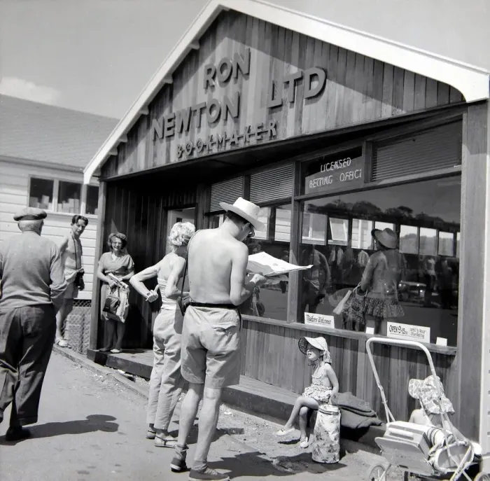 Framed Print : Holidaymakers study the form guide at a betting shop in the form of a wooden chalet Framed Print : Holidaymakers study the form guide at a betting shop in the form of a wooden chalet