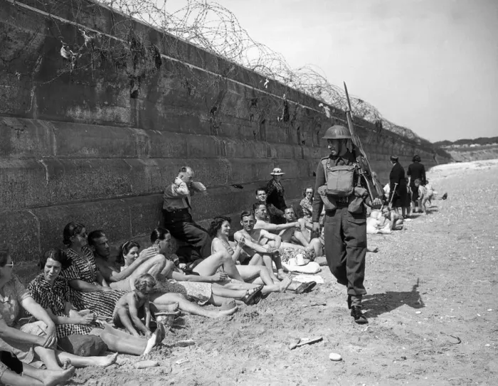 Framed Print : Holidaymakers sunbathing look pityingly at a passing home front serviceman carrying a Framed Print : Holidaymakers sunbathing look pityingly at a passing home front serviceman carrying a