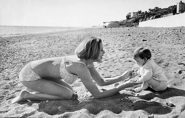 Honor Blackman wearing biini playing with daugher Lottie on beach in Spain during filming