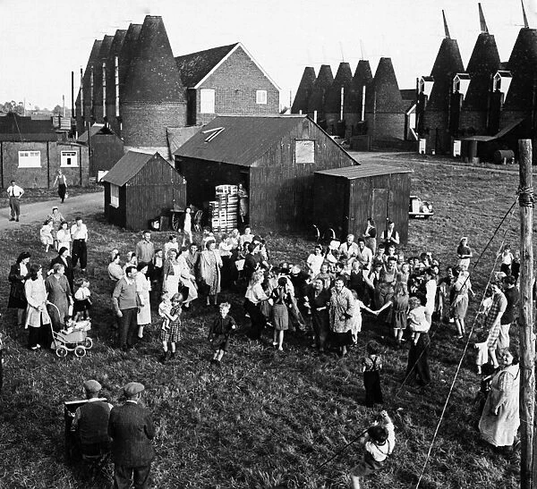 Hop pickers gathered in a Kent village with oast houses in the background, circa 1930