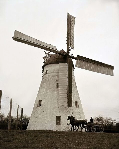 Horse and cart passing by a windmill in the English countryside circa 1950s