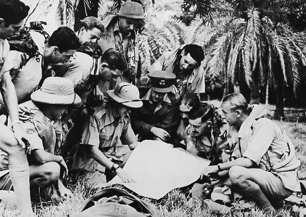 A Hudson crew operating over Burma. In a jungle clearing an RAF engineer briefs a