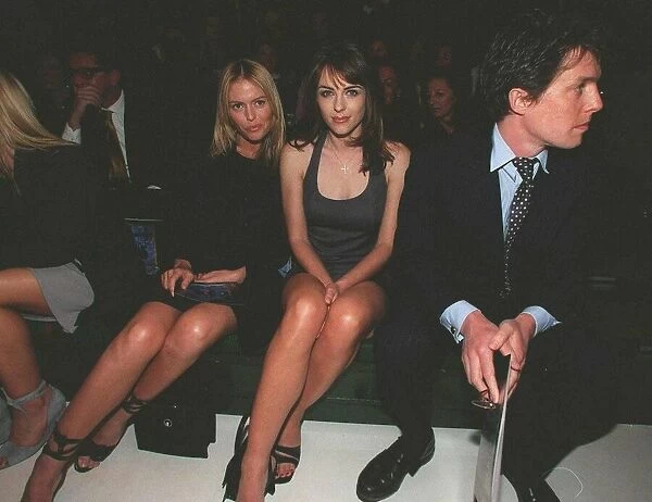 Hugh Grant actor with girlfriend Liz Hurley sits on bench to watch the Versace fashion