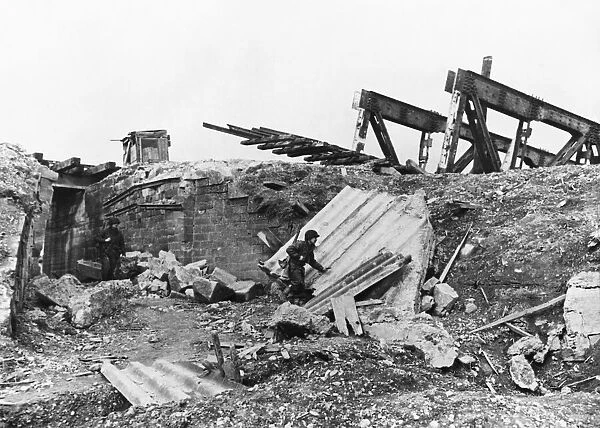 Two infantry men on patrol pass under a blown up approach to a railway bridge of