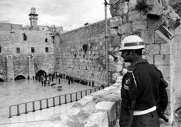 An Israeli soldier stands guard while Jewish people worship at the ancient wailing wall