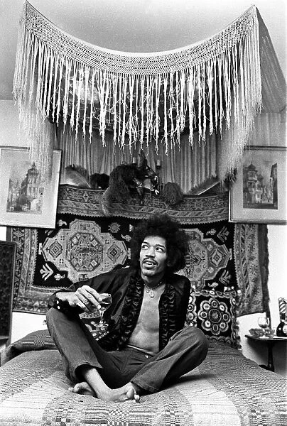 Jimi Hendrix, world famous guitarist, sitting on bed wearing open shirt and necklace