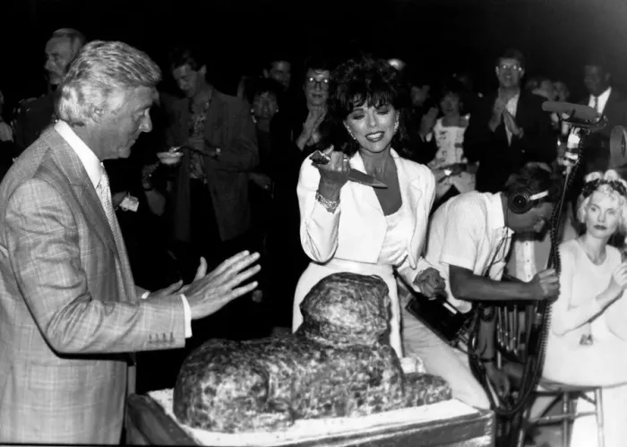 Framed Print : Joan Collins Actress frowning at cutting the cake in the shape of a Sphinx