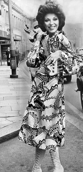 Joan Collins carrying electric guitar at the Extravaganza 70s fashion exhibition at