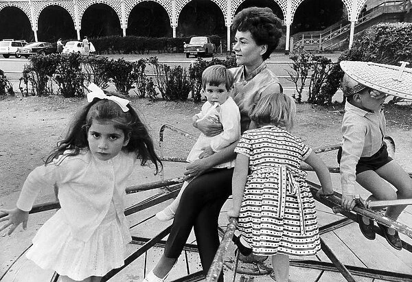 Joan Plowright Actress sitting on merry go round holding child with other children