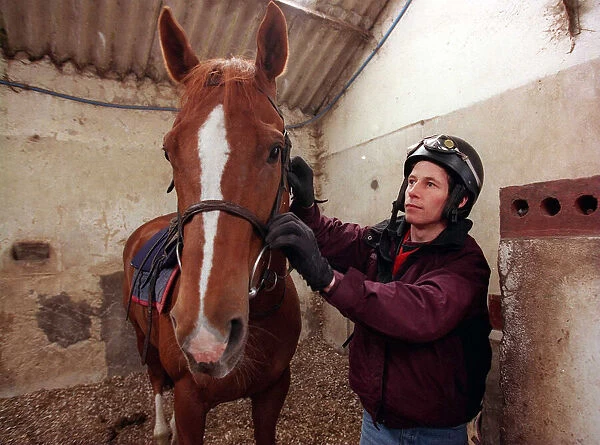 Jockey John McAuley cleaning bridle of the horse Serious Hurry in stables, June 1988