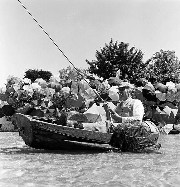Joe Carver, owner of an umbrella making business, sits in a fishing boat smoking a cigar