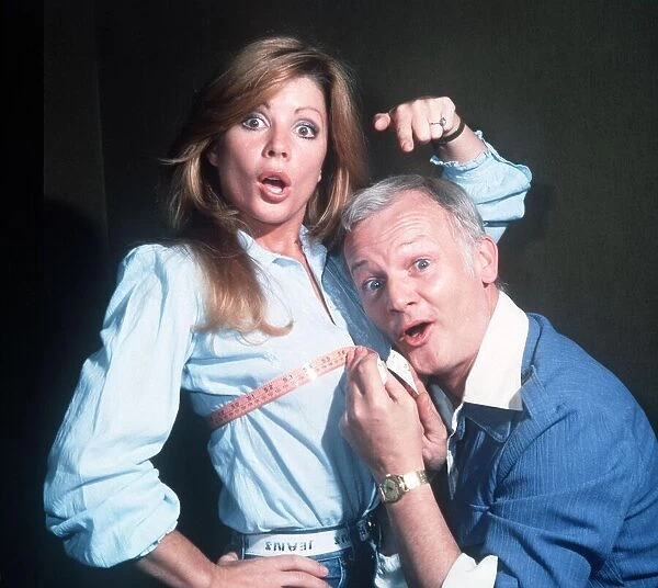 John Inman Comedian Actor holds a tape measure around the chest of Actress Penny Irving