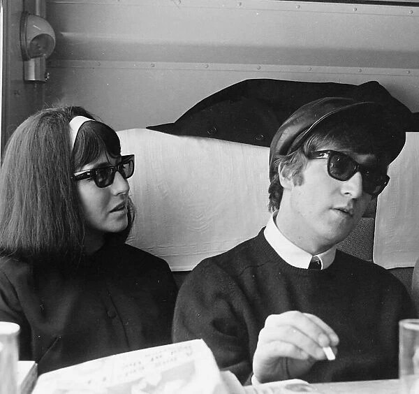 John Lennon and Cynthia Lennon wearing a dark wig over her blonde hair sitting on a train