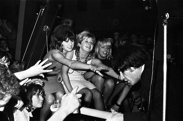 The Kinks on stage during a concert, watched by adoring female fans September 1964