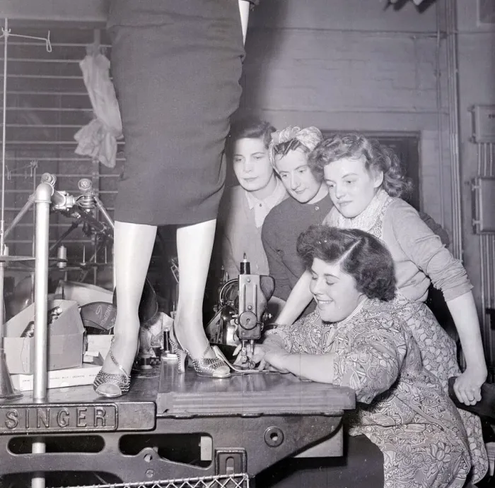 Framed Print : A lady in a pencil skirt stands on a bench while a lady sews on the sewing machine Framed Print : A lady in a pencil skirt stands on a bench while a lady sews on the sewing machine